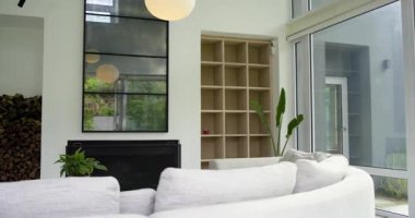 Başlangıç kamerası kıvrımlı kanepenin üzerinde dönüyor oturma odası düzenini vurgulamak için bahçe manzarasını gözler önüne seriyor. Modern, minimalist, rahat, zarif, doğal, davetkar, sakin