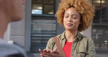 Afro-Amerikalı bir kadın kahverengi çantalı bir arkadaşıyla konuşuyor ve el çırpıyor. Kentsel, yaşam tarzı, samimi, canlı, iletişim, arkadaşlık, adaylık