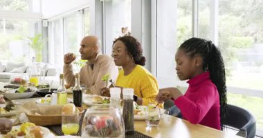Çeşitli aileler baba jestine tepki veriyor, salata dağıtıyor, ekmek batırıyor, masada meyve suyu içiyor. Aile, yemek, birliktelik, beslenme, açık hava, doğal ışık, ev