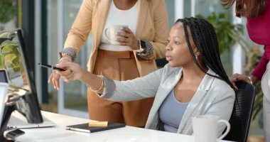 Ofis monitöründeki izleme çizelgesi siyah kadının stilus rehberlik takımını işaret ederek not defterine not bırakıyor. İşbirliği, takım çalışması, modernlik, profesyonel, beyin fırtınası, stratejik, üretkenlik