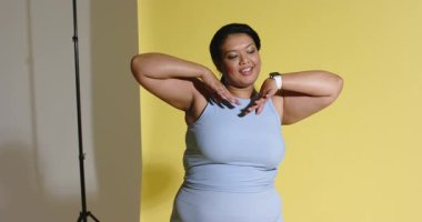 30 'lu yaşlarda Asyalı bir kadın stüdyoda gülümseyen bir ukalanın altını çizerek bileklerini çeviriyor. Fitness, sağlık, zarafet, hareket, aktif giysi, teknoloji, stüdyo