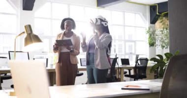 VR kulaklık takan Afro-Amerikalı kadın geliştiriciler ofiste tablet ile arayüzü kontrol ediyorlar. İşbirliği, yenilik, teknoloji, takım çalışması, dijital, geleceksel, çalışma alanı