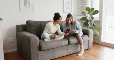 Çeşitli bayan arkadaşlar tablet bükerek, oturma odasındaki kanepede bardakları tıkırdatarak ve yudumlayarak. Gündelik, dostluk, iletişim, modern, rahat, yaşam tarzı, boş zaman