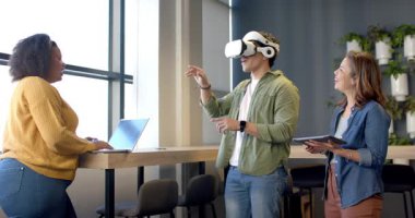 VR 'a giriyoruz, kulaklık takan adam masada meslektaşlarıyla birlikte elementleri büyütüyor. Yenilik, işbirliği, teknoloji, dijital, etkileşim, çalışma alanı, gelecekçilik