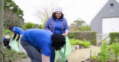 Çeşitli gönüllüler yeşil torbaları açıp yabani otları topluyor ve onları bahçe temizliği için dolduruyor. Topluluk, işbirliği, sürdürülebilirlik, açık hava, çevre, yeşillik, takım çalışması