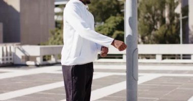 Spor giyimli Afro-Amerikalı bir adam çatıdaki direği kullanarak bacak ve omuz germe hareketleriyle ısınıyor. Fitness, esneklik, açık hava, şehir, motivasyon, sağlık, duruş