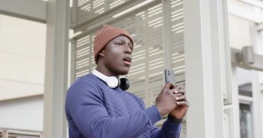 Afro-Amerikalı bir adam sığınakta akıllı telefonları kaydırıyor, gürültüye cevap veriyor, okumaya devam ediyor. Kentsel, teknoloji, gelişigüzel, modern, iletişim, şehir manzarası, yaşam tarzı