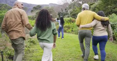 Yürüyen bir aile grubu, gri evi gören ve çimlere doğru koşan kızlarıyla yolda sohbet ediyor. Açık hava, arkadaşlık, kırsal alan, yaşam tarzı, uyum, rahatlık, doğal