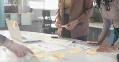 Tasarım notuna işaret eden çeşitli bayan meslektaşlar, masa planlama çizelgelerini gözden geçiriyorlar. İşbirliği, takım çalışması, analitik, sunum, beyin fırtınası, yenilik, verimlilik