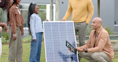 Erkek teknisyen, Afrikalı Amerikan ailesi için güneş hücrelerini gösteren tablet tıkırdatıyor. Yenilenebilir, sürdürülebilirlik, eğitim, teknoloji, açık hava, modern, neşeli