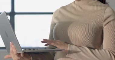 Elinde gümüş dizüstü bilgisayar tutan, daktilo eden, ekranı okuyan ve ofiste gülümseyen yetişkin bir kadın. Profesyonel, teknoloji, modern, işyeri, üretkenlik, şirket, iş kadını