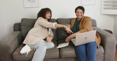 Çeşitli bayan arkadaşlar ellerinde kupalarla kanepeye gülen bilgisayarları incelemek için belgeye işaret ediyorlar. İşbirliği, gündelik, modern, iletişim, iç mekan, rahatlık, pozitiflik