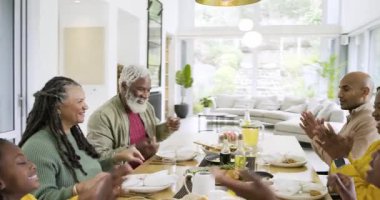Çeşitli aileler el ele tutuşup dua ediyor, peçeteleri açıyor ve yemek odasında kızarmış tavuk servis ediyor. Çoklu nesil, birliktelik, kutlama, sıcaklık, uyum, yerli, kırsal