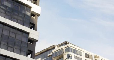 Kamera yukarı doğru eğilmiş, yüksek katlı ön cephe soluk mavi gökyüzüne karşı balkonlardan tırmanıyor. Gökdelen, mimari, kentsel, modern, şehir manzarası, geometrik, cam cephe