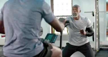 Kıdemli Afro-Amerikan erkek koç, spor salonunda kürek çeken ekran koçunu işaret ediyor. Fitness, koçluk, spor salonu, güç, eğitim, motivasyon, disiplin