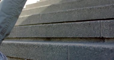 Erkek ayakkabıyı merdivene doğru itiyor, yukarı doğru kayıyor, yere doğru somut adımlar atıyor. Ayakkabı, açık hava, şehir, ilerleme, hareket, gündelik, mimari