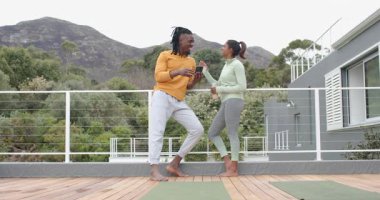 Telefon dinleyen çeşitli arkadaşlar dağ güvertesinde su şişesi tutan yoga rutinini gözden geçirecekler. Açık hava, yoldaşlık, doğal rahatlama, fitness, takım çalışması, yaşam tarzı.