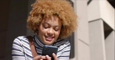 Afrika kökenli Amerikalı bir kadın, akıllı telefonları dinleyerek alarm üstüne alarm veriyor, modern görüntünün dışında gülümsüyor. Gündelik, açık hava, çağdaş, mimari, teknoloji, yaşam tarzı, neşeli