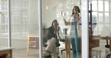 Çeşitli kadın iş arkadaşları cam tahtaya proje diyagramı yazma stratejisi belirliyor. İşbirliği, beyin fırtınası, takım çalışması, yenilik, modernlik, üretkenlik, iletişim