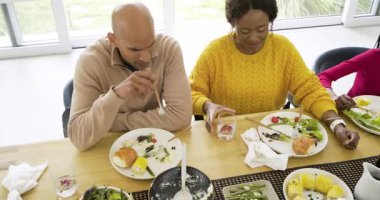 Tabaklar temizlendikten sonra, çeşitli aileler masaya gülümserken tabakları doldurmak için salata kâselerini uzatırlar. Aile, birliktelik, yemek, doğal ışık, sıcaklık, kutlama, bağlantı