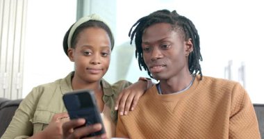 Gelen aramalardan sonra Afro-Amerikalı çift ellerinde kahve fincanlarıyla kanepede el sallıyorlar. Çift, iletişim, rahatlama, ev, yaşam tarzı, rahat, teknoloji