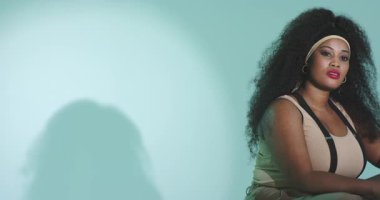 Stüdyo ışığı Afrikalı Amerikalı kadının kameraya dönüp tabureye gülümsemesine neden oluyor, kopyalama alanı. Portre, profesyonellik, minimalist, güzellik, güven, moda, zarafet