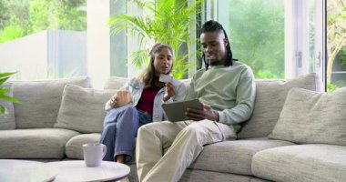 Kanepede oturan, kredi kartı tutan, siparişi onayladıktan sonra tableti tıkırdatan bir çift. Modern, rahat, yaşam tarzı, rahatlama, teknoloji, bağlantı, mutluluk