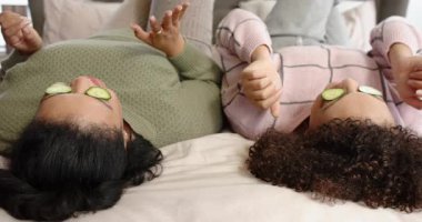 Çeşitli bayan arkadaşlar salatalık dilimlerini ayarlıyor dizlerini kaldırıyor ve spa için yatakta el ele tutuşuyorlar. Rahatlama, dostluk, refah, rahatlık, rahatlık, samimiyet, minimalist