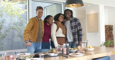 Dört arkadaş kameraya gülümsüyor, sarılıyor ve gülüyor. Kahvaltıyı ahşap yemek masasının etrafında paylaşıyorlar. Arkadaşlık, dostluk, kutlama, birliktelik, sosyal toplanma, samimi, neşeli