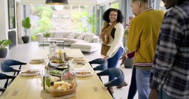 Arkadaş grubunu yemek odasına götüren kapı açılıyor, ahşap masadaki sebze kaselerini işaret ediyor. İşbirliği, konukseverlik, kırsal, modern, kutlama, sıcaklık, konukseverlik