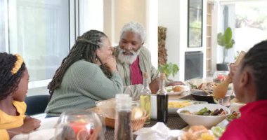 Afro-Amerikan ailesi salata servisi yapıyor, yemek alanında sohbet ediyorlar, kadın kocasının elini tutmaya çalışıyor. Aile, mutfak, birliktelik, modern, ev, sıcak, gayri resmi