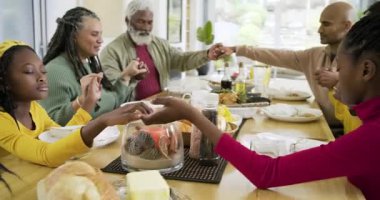 Üç nesildir yemek masasının etrafında el ele tutuşan ve yemekten önce alkışlayan bir aile. Aile, gelenek, birliktelik, minnettarlık, bağlantı, kutlama, sıcaklık