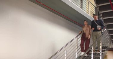 Çeşitli iş arkadaşları ofis merdivenlerinden iniyorlar, ellerinde ray ve laptop tutuyorlar, konuşuyorlar, kopyalama alanı oluşturuyorlar. İşbirliği, profesyonellik, takım çalışması, modern mimari, kurumsal, iletişim, çeşitlilik