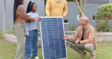 Teknisyen bağlayıcıyı gösteriyor ve avludaki panelleri birbirine bağlayan Afrikalı Amerikalı aileyi yönlendiriyor. Yenilenebilir, sürdürülebilir, yenilikçi, çevre dostu, eğitim, açık hava, modern