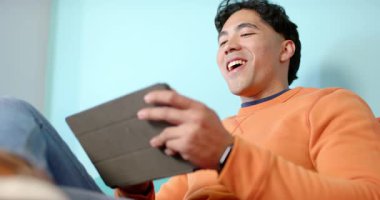 Kucaktan siyah tableti kaldıran, dokunmatik ekranı tıklatan ve koltukta komik klipsleri izleyen bir adam. Teknoloji, rahatlama, eğlence, gündelik, yaşam tarzı, modern, dijital