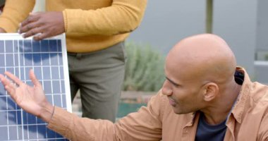 Afrikalı Amerikan ailesi avluda diz çöken teknisyenler olarak güneş paneli hücrelerini öğreniyor. Yenilenebilir enerji, aile, teknoloji, açık hava, yenilik, sürdürülebilirlik, eğitim