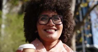 Afro-Amerikalı kadın elinde kahve fincanı tutarken gülümsüyor, gün ışığında başını sağa çeviriyor. Neşe, rahatlama, tazelik, canlılık, gündelik, kentsel, doğa