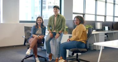 Çeşitli iş arkadaşları fotoğrafçı işareti alıyor, koltukları değiştiriyor, açık ofiste gülüyor ve gülümsüyor. İşbirliği, takım çalışması, çeşitlilik, modern, profesyonel, gündelik, arkadaşlık