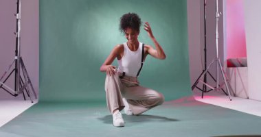 Stüdyoda yeşil arka planda poz veren rahat giyinen kendine güvenen bir kadın. Moda, tarz, portre, kadın, tutum, çağdaş