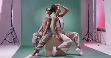 Moda kıyafetleri ve güneş gözlükleriyle stüdyoda güven içinde poz veren iki şık kadın. Moda, tarz, güven, cazibe, şıklık, zarafet.