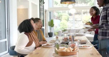 Çeşitli arkadaşlar evde yemek masasında salata kasesi taşıyan ev sahipleri gibi alkış tutuyorlar. Toplanma, kutlama, neşe, sıcaklık, zarafet, sosyal etkileşim, iç mekan