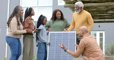 Güneş panelini inceleyen çeşitli aile ve güneş teknisyenleri ön bahçeyi tartışırken. Yenilenebilir, sürdürülebilirlik, yenilik, eğitim, teknoloji, çevre dostu, modern