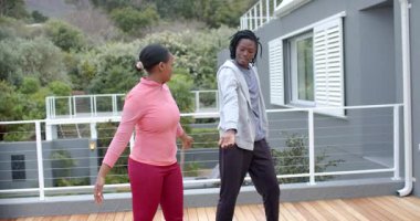 Afro-Amerikan spor kıyafetleri içinde antrenman arkadaşları güvertede rehberlik ediyor ve yan esneme hareketleri yapıyorlar. Açık hava, fitness, aktivite, rahatlama, doğa, sağlık, hareket