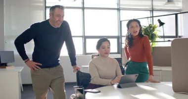 Çeşitli iş arkadaşları tablette buluşmaya başlıyor, eğiliyor ve ekranı işaret ediyor, ofiste hemfikir oluyorlar. İşbirliği, erişilebilirlik, takım çalışması, dijital, çeşitlilik, profesyonel, yenilik