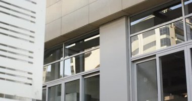 Solda görünen beyaz delikli panel güneşli gökyüzünün altındaki pencereleri kaplayan ön cephede kayıyor. Modern, mimari, tasarım, cephe, inşaat, yapı, şehir