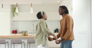 Afro-Amerikalı çift el ele tutuşuyor ve gülümserken mutfak adasında sallanıyorlar. Romantizm, samimiyet, bağlantı, uyum, neşe, hareket, modern