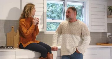 Mutfakta sohbet eden çiftler, kadın kaldıran ve bardaklarını yudumlayan erkekler tezgaha yaslanıp dinlerken. Konfor, samimiyet, aile içi, sohbet, samimiyet, bağlılık, yaşam tarzı