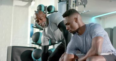 Afrika kökenli Amerikalı antrenör, spor salonunda 10 kiloluk bir halteri kaldırırken yumruğunu sıkıyor. Eğitim, akıl hocalığı, güç, motivasyon, fitness, dayanıklılık, koçluk.