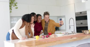 Çeşitli arkadaşlar tezgah tezgah yemek yapıyor, selfie için telefon kaldırıyor ve fotoğrafları gözden geçiriyorlar. Samimi, yaşam tarzı, günlük, iç mekan, topluluk, neşeli, otantik