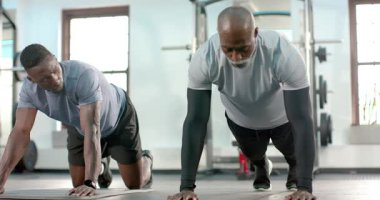 Afrikalı Amerikalı antrenör diz sürüşünü başlatıyor, müşteri spor salonundaki paspaslarda çekirdek dayanıklılık için dizlerini eşleştiriyor. Fitness, strength, exercise, interval training, athletic, motivasyon, energy